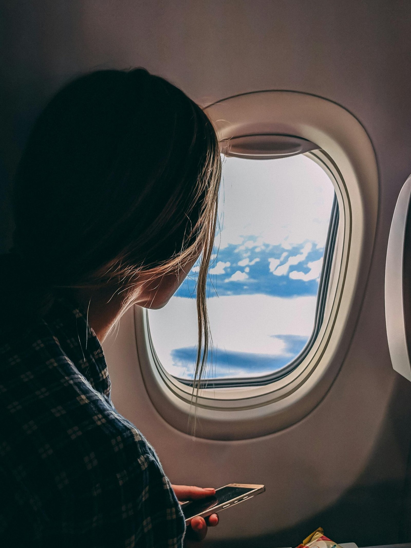 Picture of a lady holding her smartphone and looking through the window of an airplane on the air