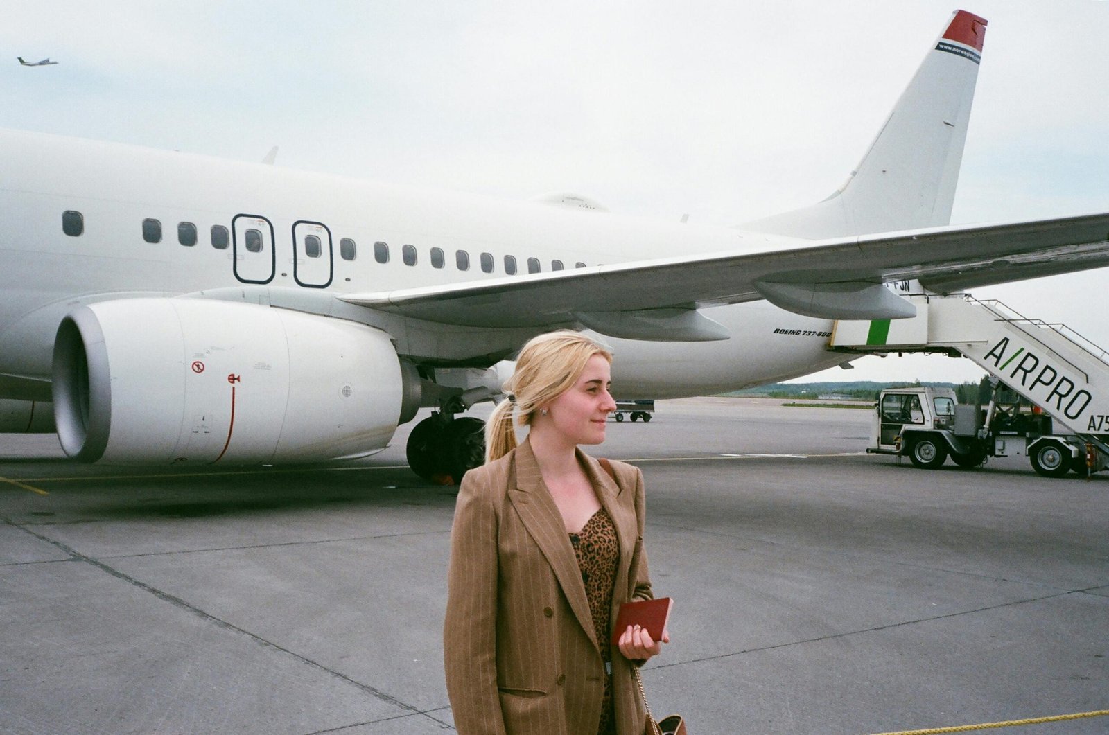 Smiling female tourist with her passport near airplane at the airport