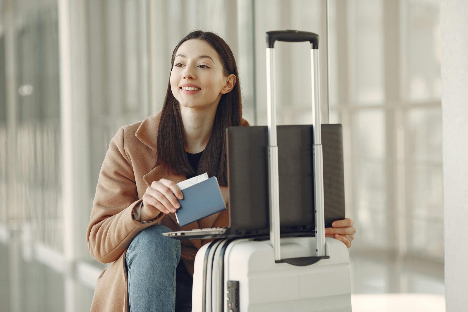 Picture of a happy woman with passport using laptop on luggage in airport