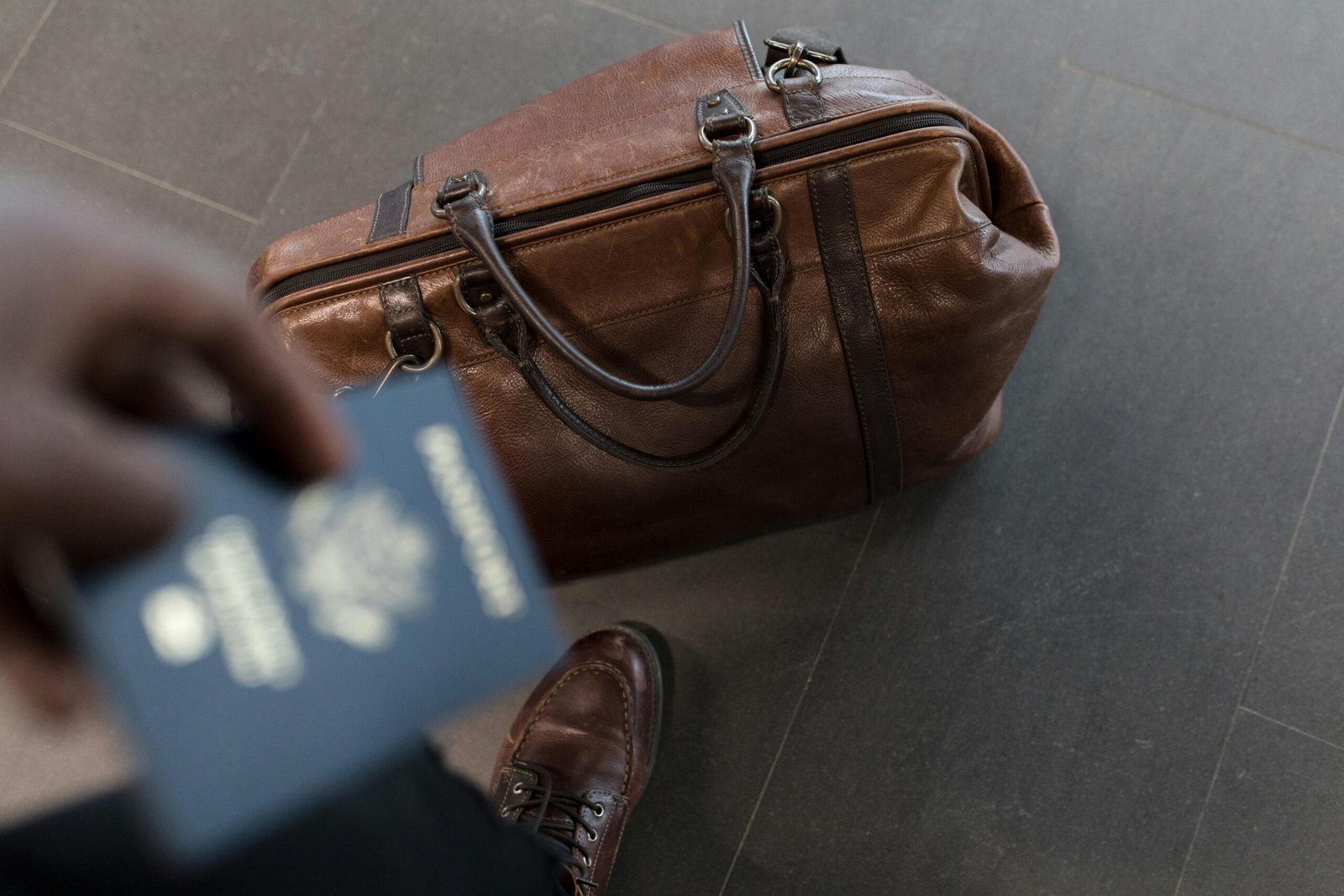 A traveler carrying Brown Leather Duffel Bag with his passport
