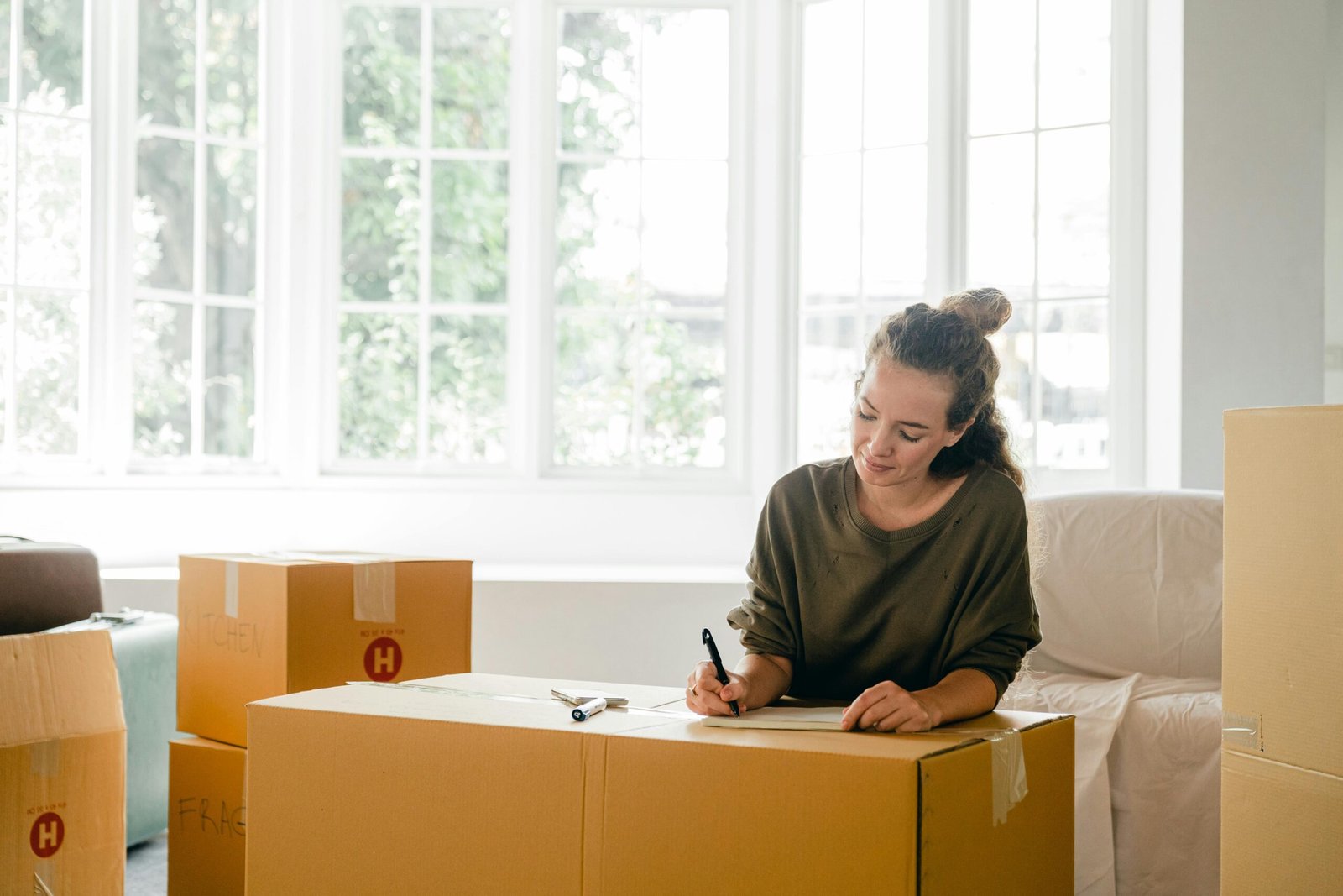 Woman signing packed box near large window in sunlight at home